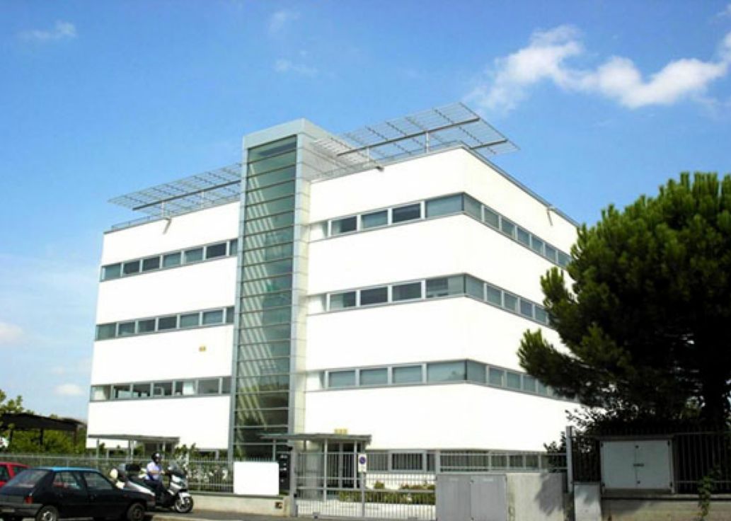 Moderno edificio per uffici bianco con vano scale in vetro e auto parcheggiate sotto un cielo azzurro.