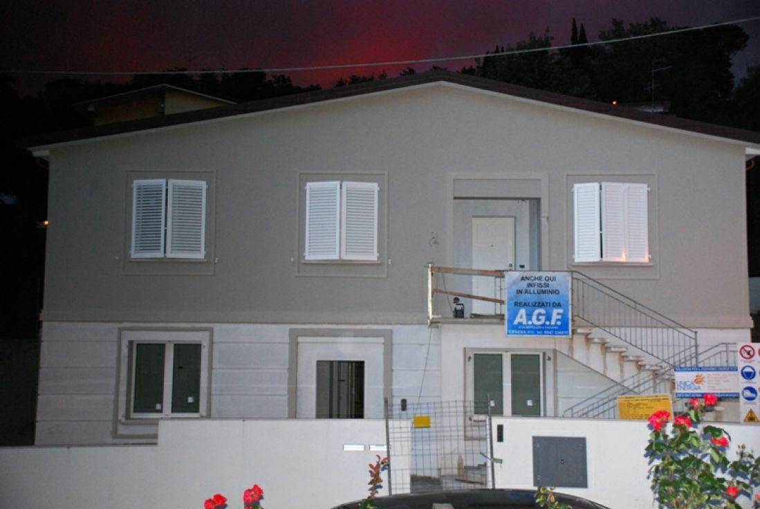 Casa a due piani al crepuscolo con esterni bianchi e grigi, scalinata d'ingresso e insegna blu AGF.