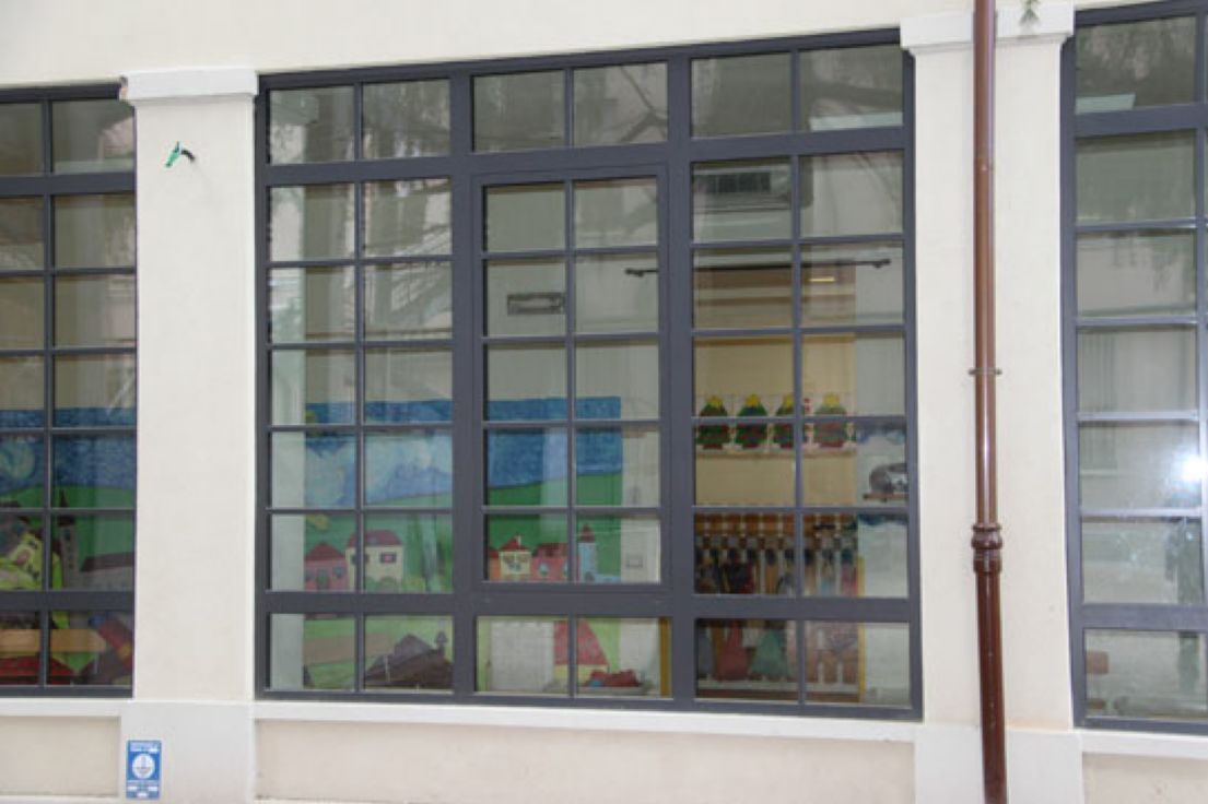 Ampia aula con grandi finestre che si aprono verso l'esterno, lasciando visibili all'interno i coloratissimi disegni dei bambini.