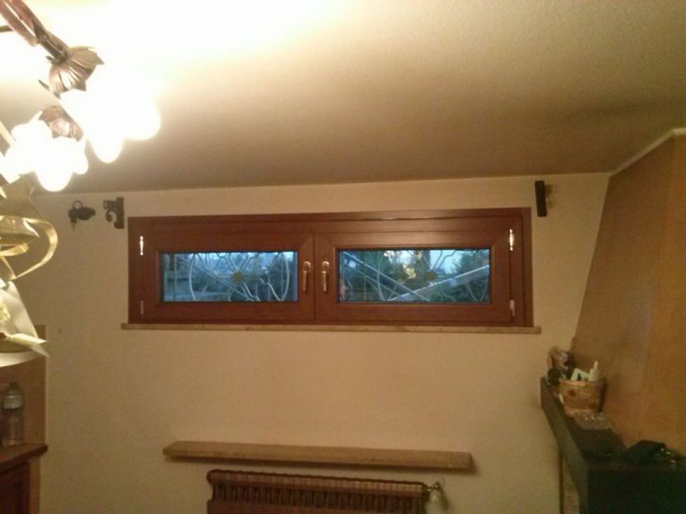 Stanza vuota color beige con una piccola finestra, copritermosifone e mensole a muro sotto una lampada a soffitto.