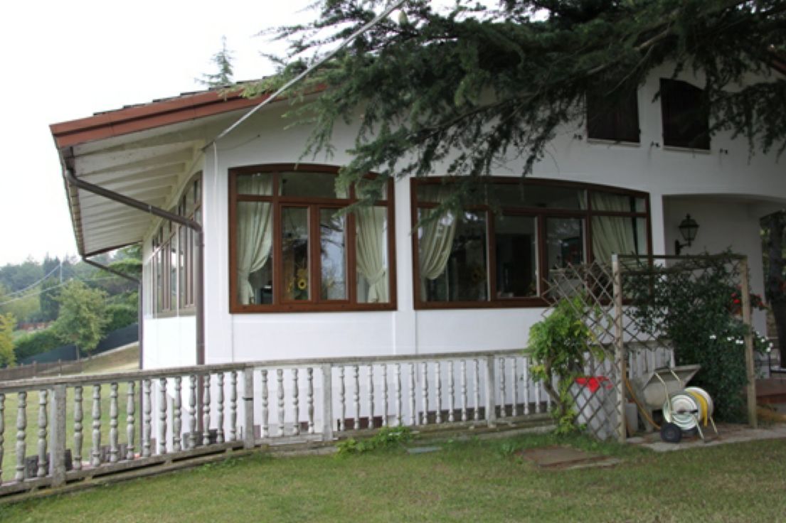 Casa bianca con grandi finestre, tetto spiovente e portico anteriore accanto a un prato e una recinzione di legno.