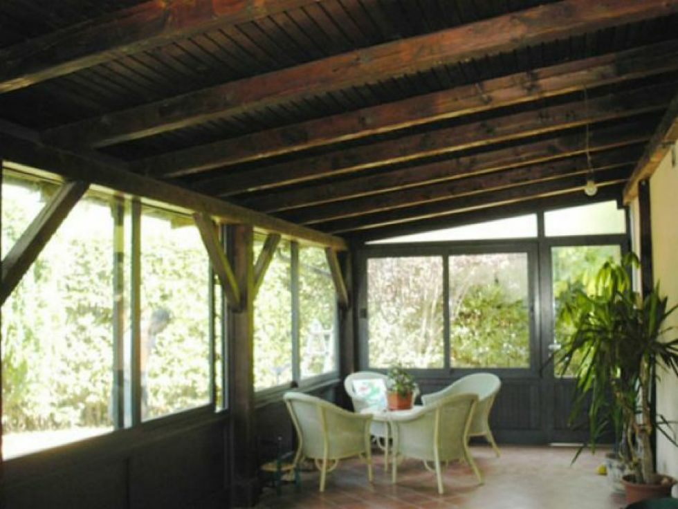 Veranda schermata con travi in ​​legno, sedie in vimini, tavolo e pianta in vaso con vista sugli alberi.
