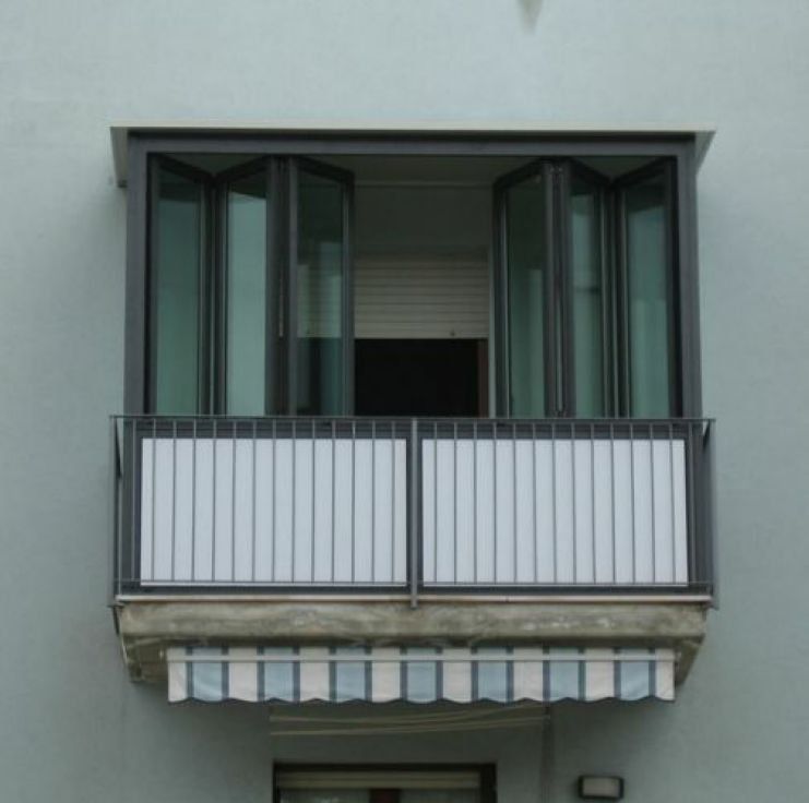 Balcone aperto con persiane e ringhiere verde scuro su una facciata chiara dell'edificio.