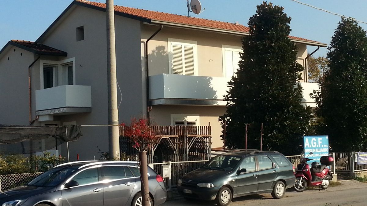 Via residenziale con auto parcheggiate e un palazzo beige con balconi e tetto rosso.