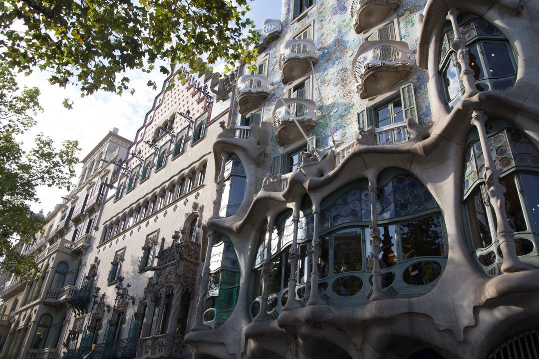 Modern curved apartment building with glass balconies and ornate stone facade under leafy trees