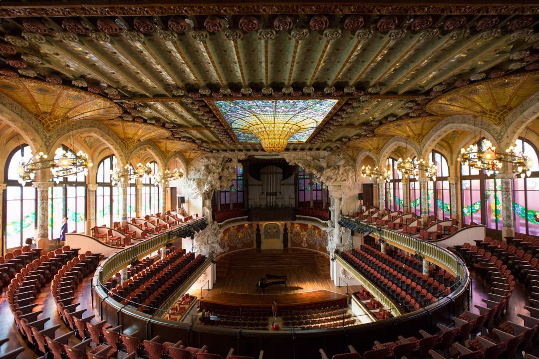 Ornate opera house interior with curved red seating, gilded arches, and a decorated ceiling