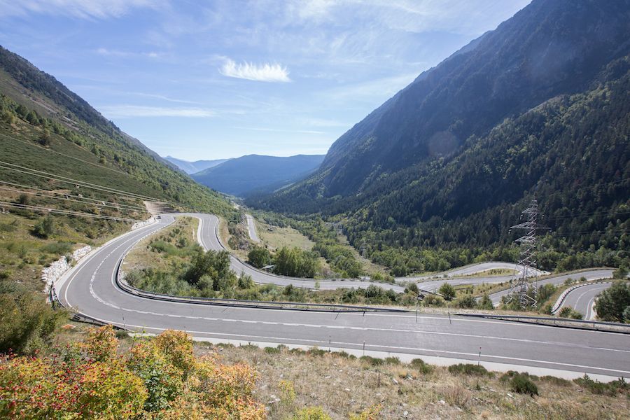 Winding mountain road through a green valley with steep rocky slopes and a distant blue horizon
