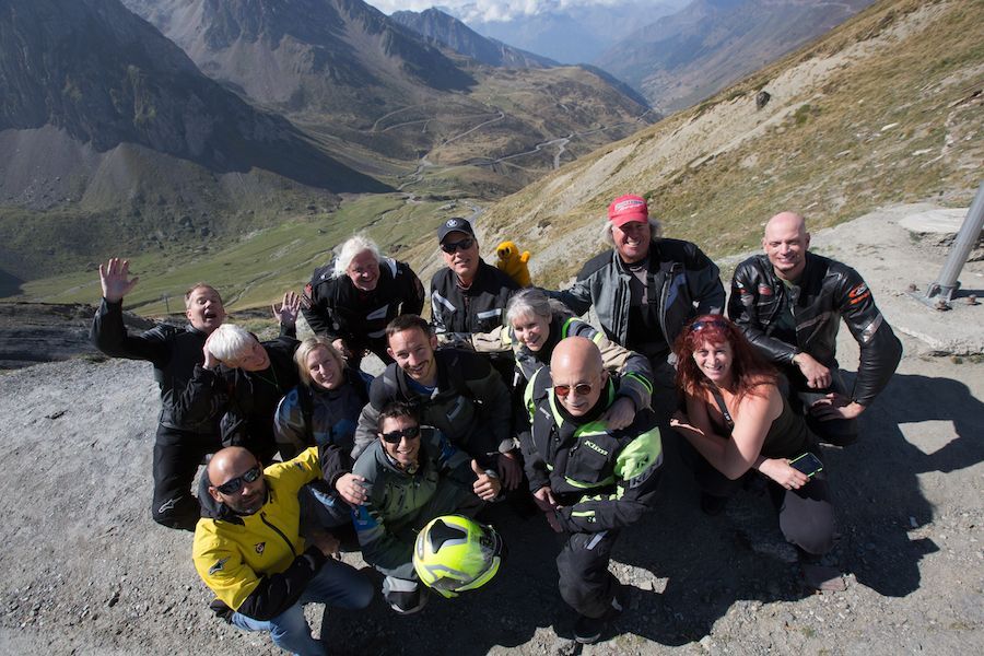 Group of hikers posing on a mountain overlook, smiling in colorful jackets with peaks and valley behind them