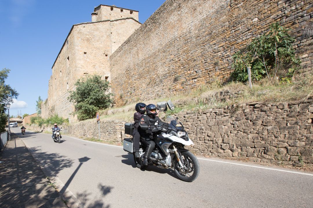 Motorcyclist riding along a narrow road beside a large stone fortress wall under a clear sky