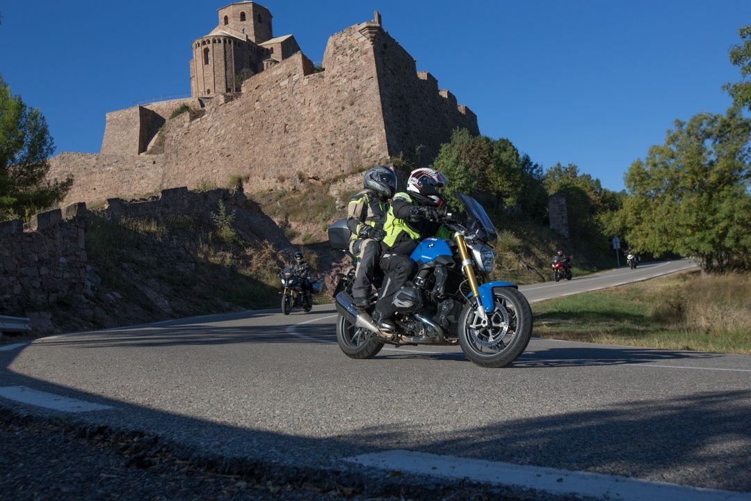 Motorcyclist riding past a stone castle on a sunny road