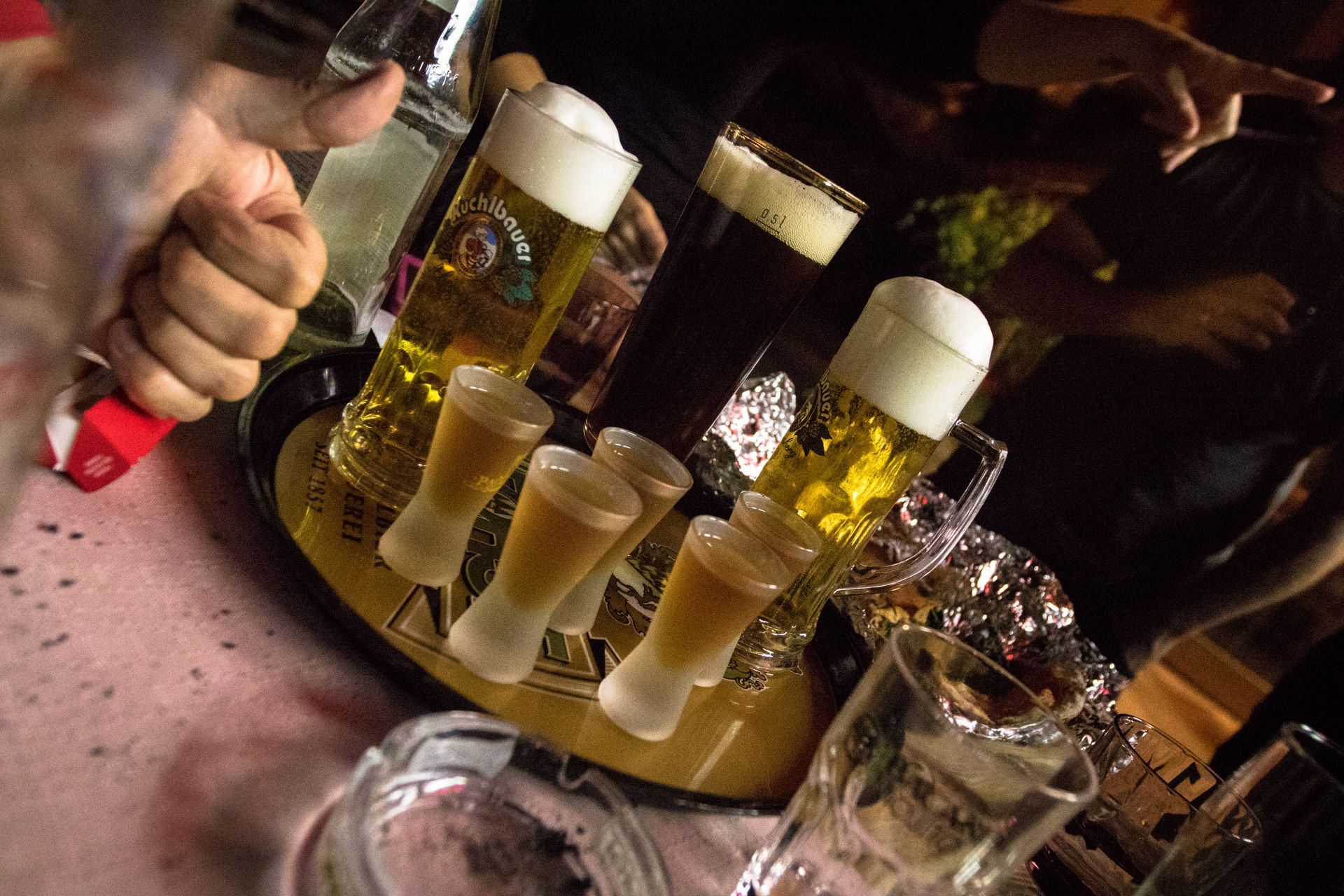 Beer glasses on a bar table with foam, surrounded by people holding drinks at a lively bar.