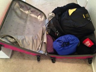 An open red suitcase packed with black and blue clothes and a gray lining