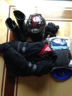 Motorcycle riding gear laid out on a table: black helmet, boots, gloves, jacket, and backpack.