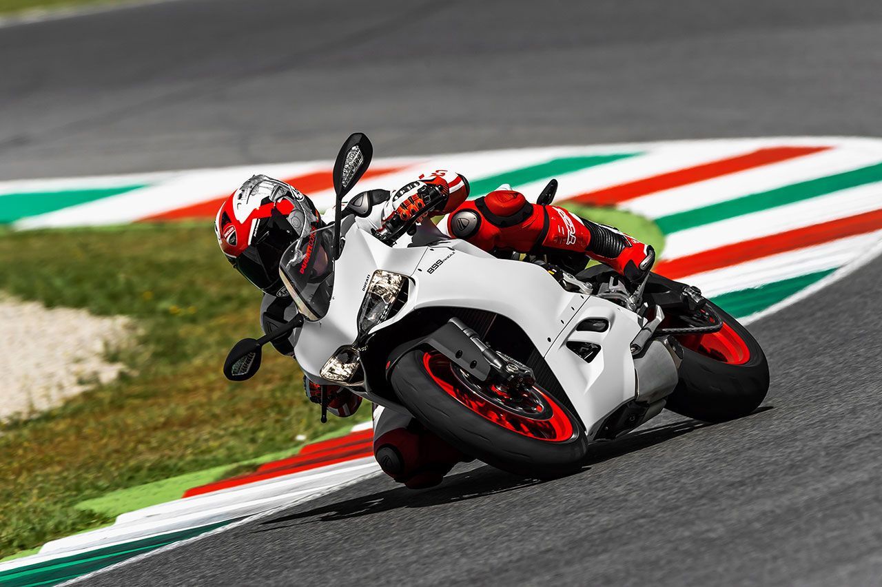 Motorcyclist leaning hard into a turn on a white racing bike on a track with red, green, and white curbs