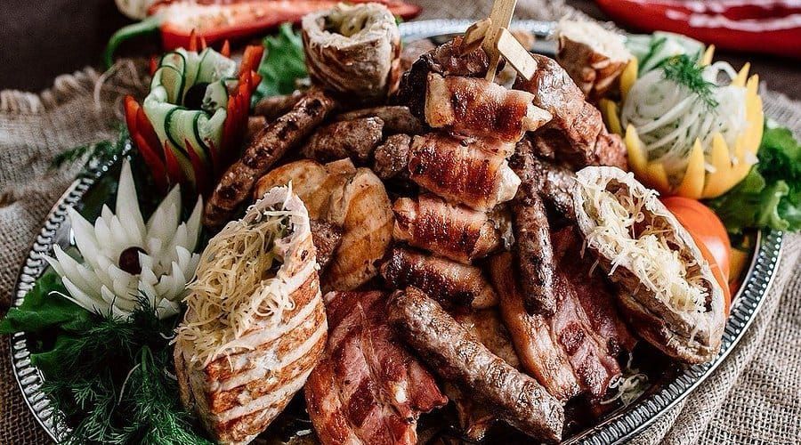 Platter of assorted grilled meats with decorative vegetables, served on a woven table setting