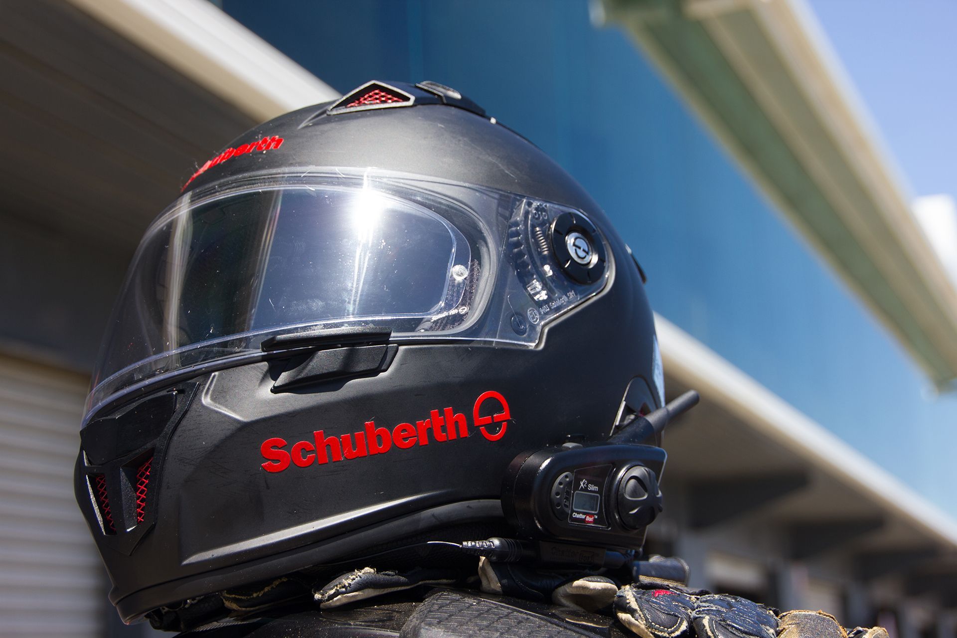 Motorcyclist in a black helmet with tinted visor, under an overpass with blue sky behind
