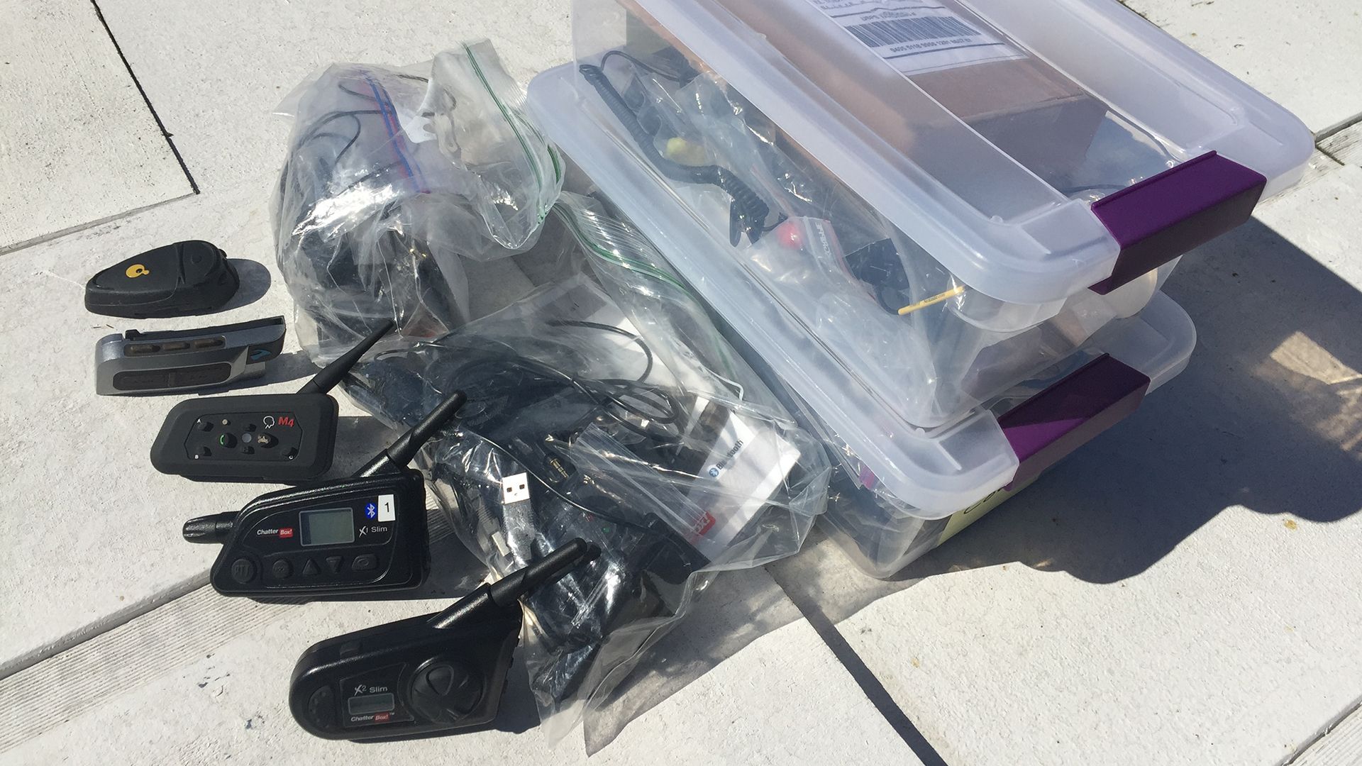 Plastic storage containers filled with black electronics and cables on a concrete surface