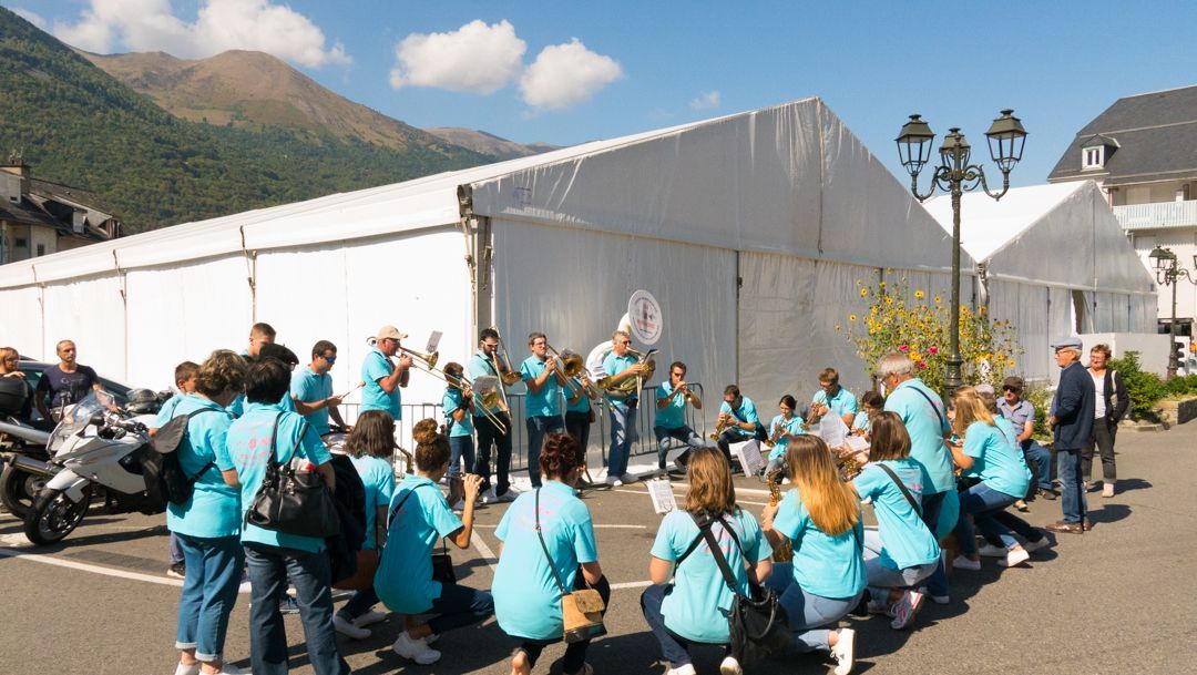 Group in teal shirts gathered outdoors beside a large white tent, with mountains and clear sky in the background