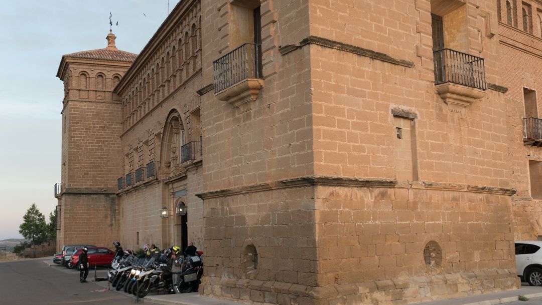 Historic stone building with tower, arched windows, and parked motorcycles along the street