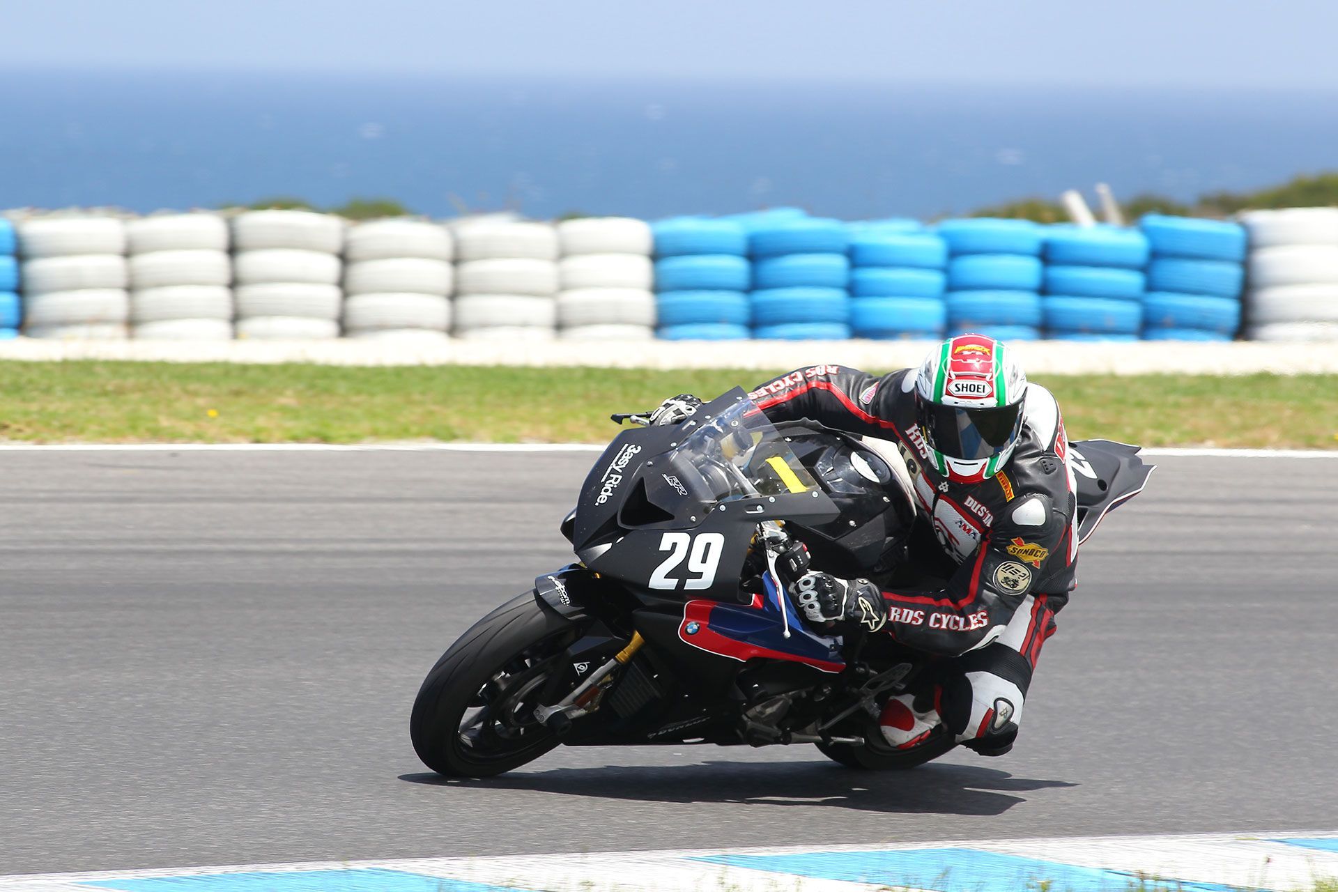 Motorcycle racer leans into a turn on a track, with blue-and-white barrier tires in the background