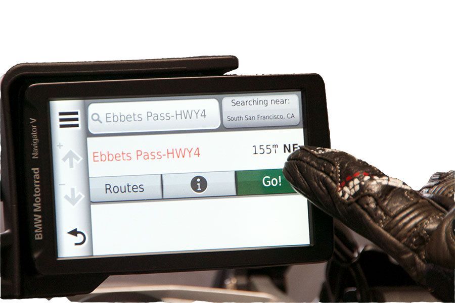 GPS navigation screen being tapped by a gloved hand, showing route search and turn directions