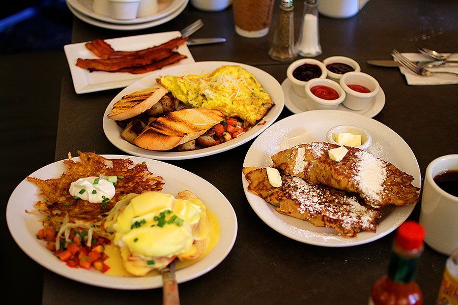 Breakfast spread with pancakes, waffles, omelet, potatoes, and dipping sauces on a table