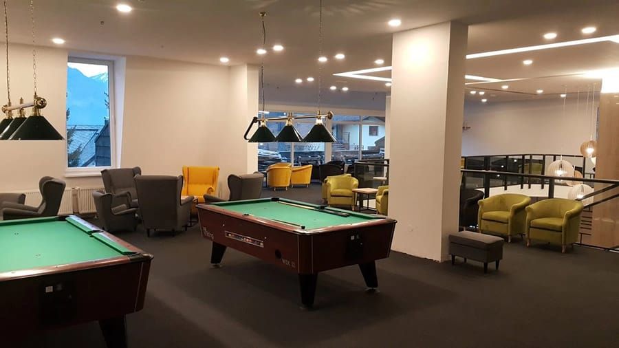 Spacious game room with pool tables, lounge chairs, and warm ceiling lights.