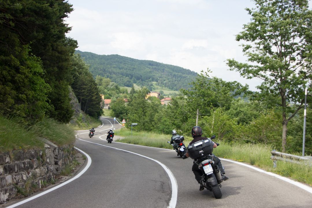 Motorcyclists riding along a winding mountain road with green hills and trees