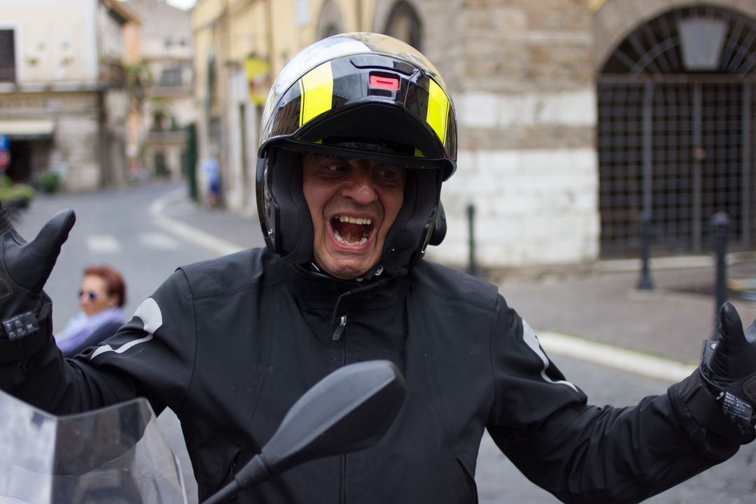 Motorcyclist in black helmet and jacket cheering on a city street, arms raised in excitement