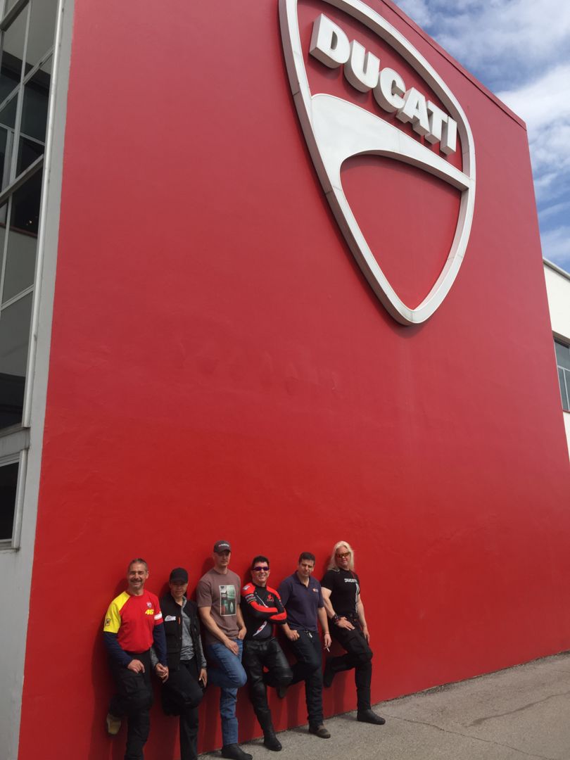 Five people pose at a red Ducati wall under a large Ducati logo.
