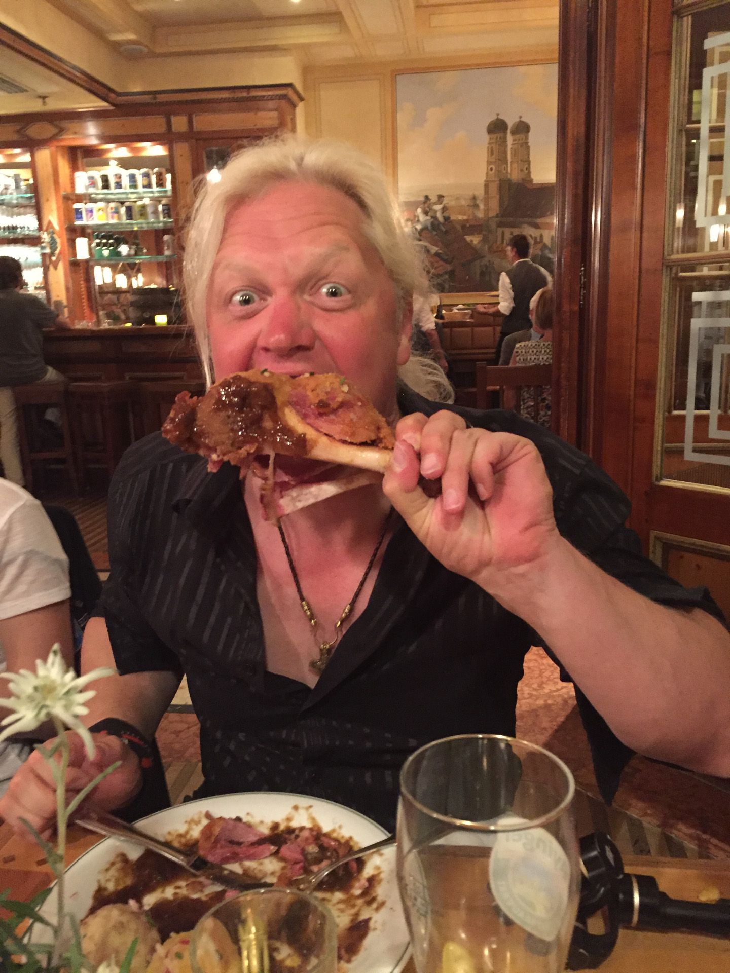 Man in a restaurant smiling while holding up a large crab leg over a plate of seafood.