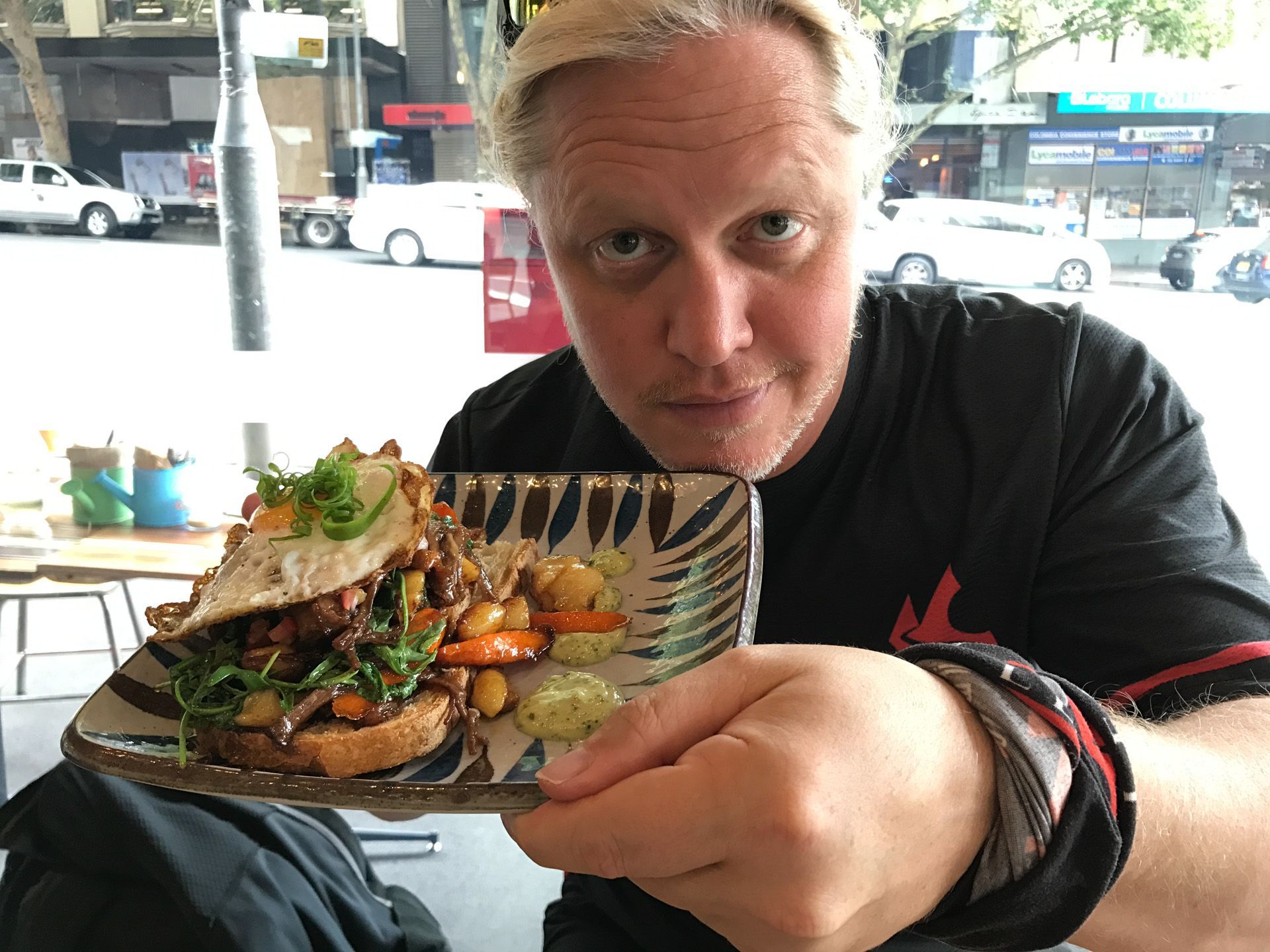 Man smiling and holding a plate of food on a restaurant patio