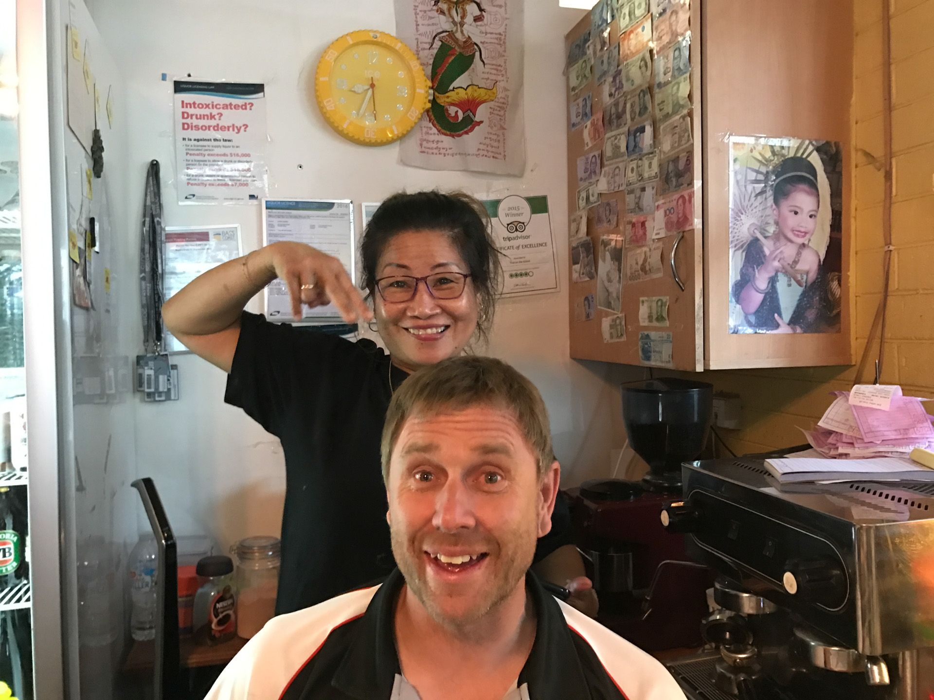 Two people smiling in a kitchen, one flexing an arm behind the other.