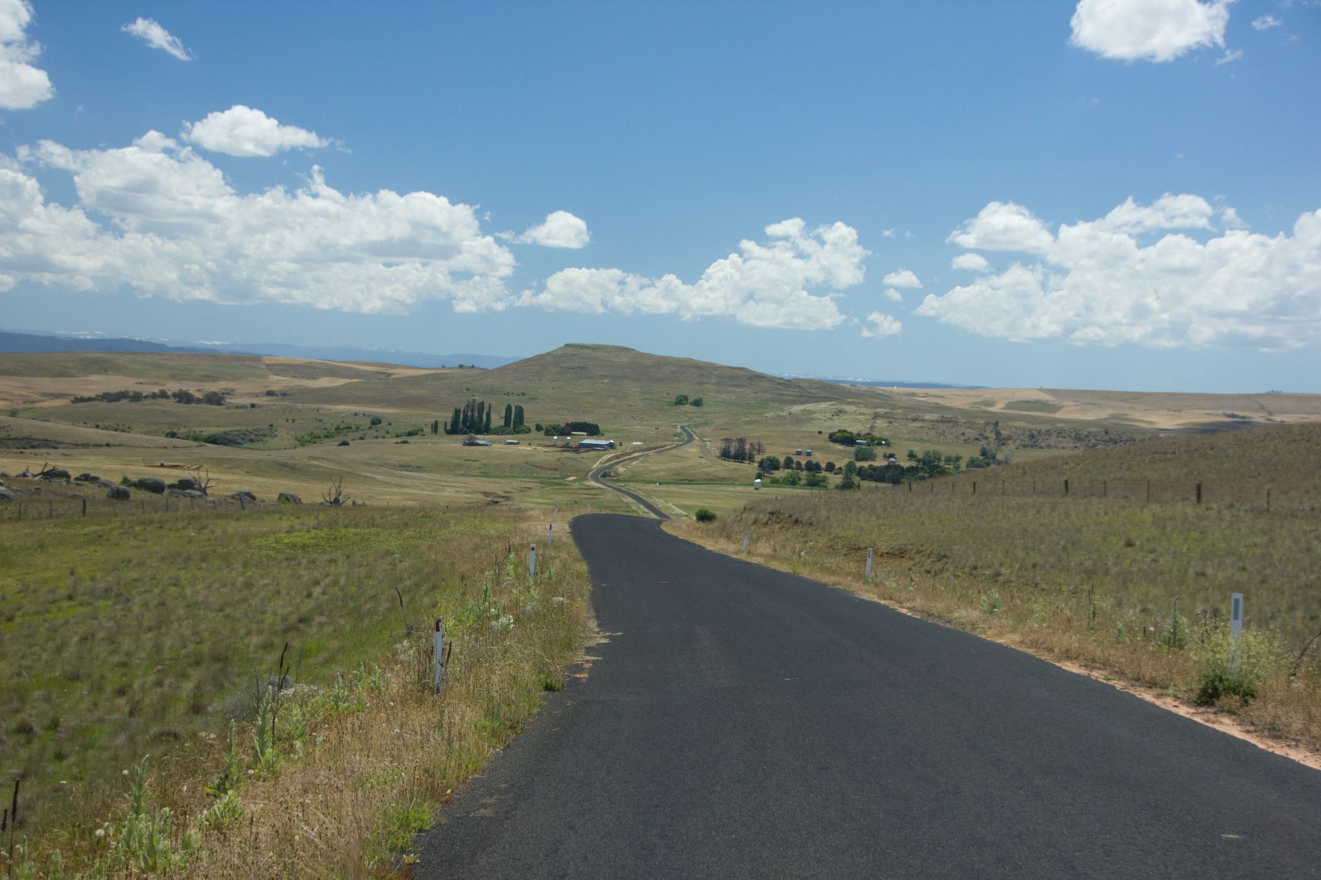 Winding paved road through dry grasslands under a blue sky with scattered clouds
