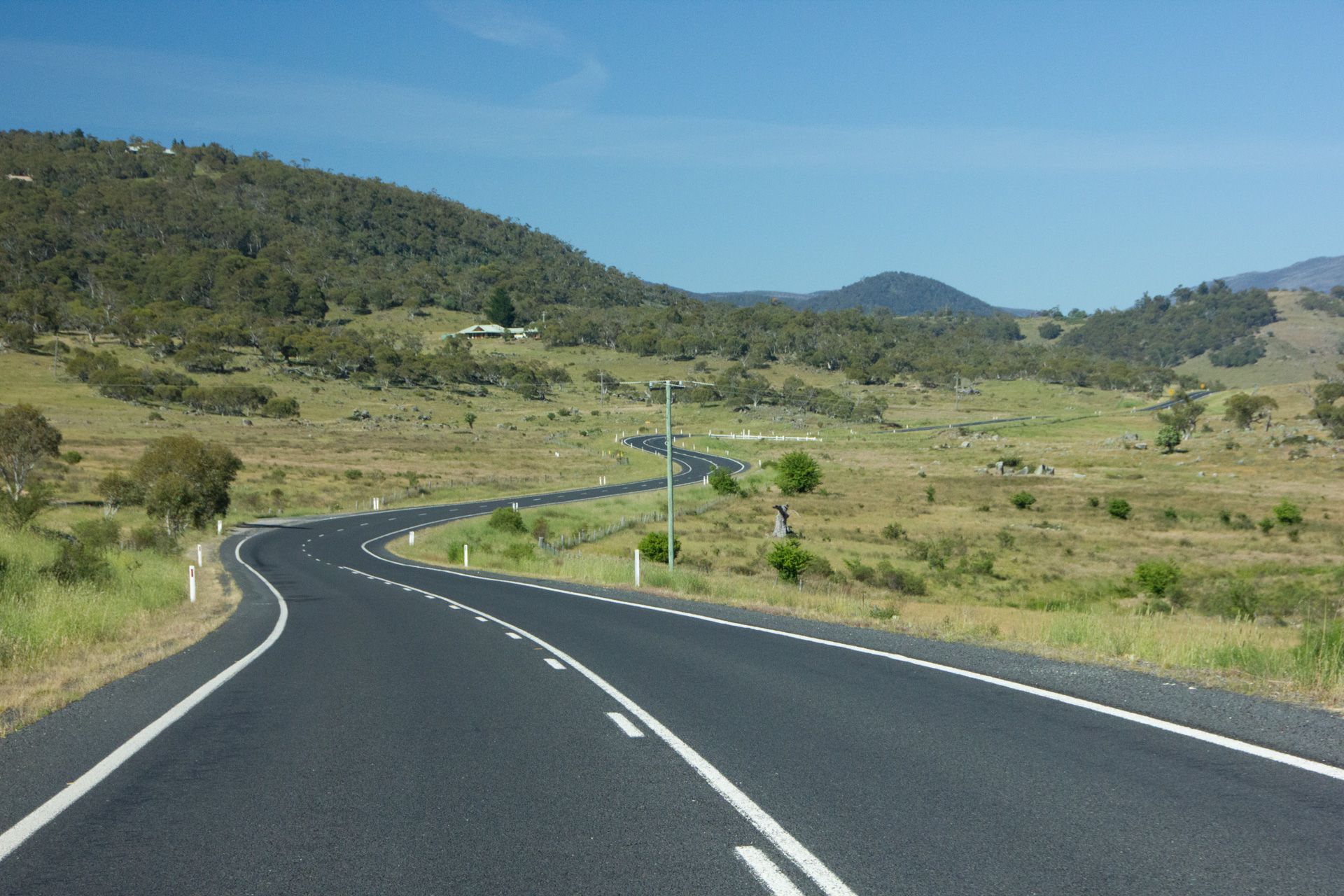 Winding paved road through grassy hills under a clear blue sky