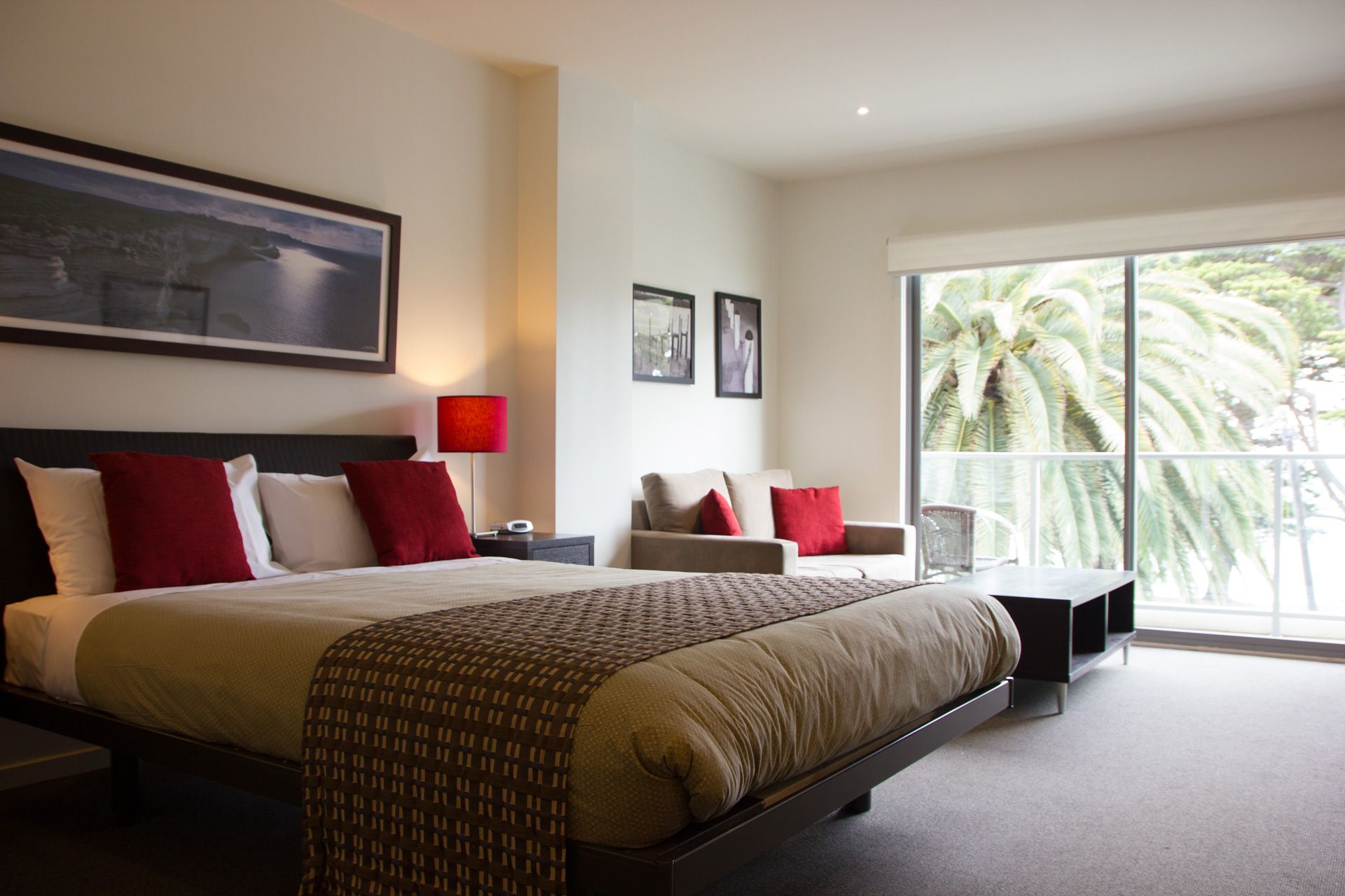 Modern hotel bedroom with king bed, red accents, and large sliding glass doors to a tropical view