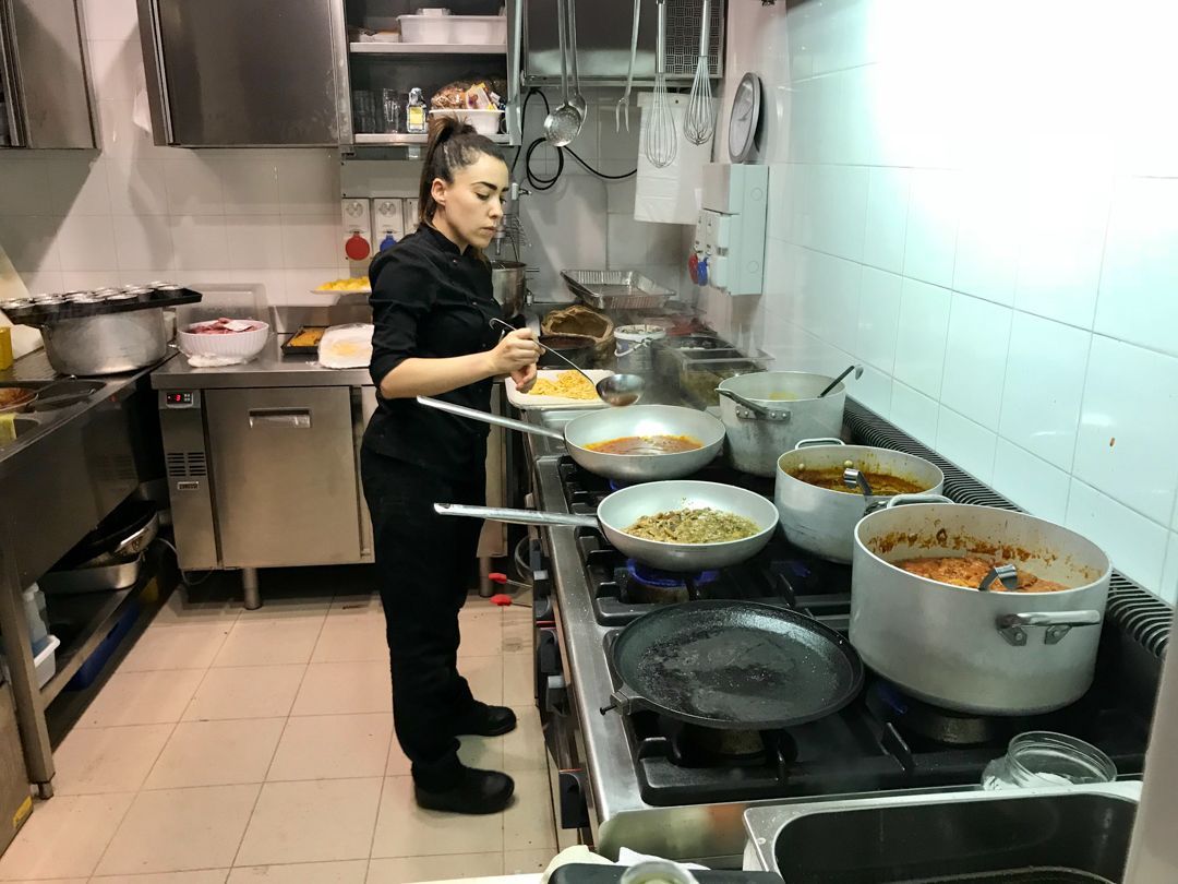 Chef cooking in a busy kitchen, stirring food in several pots on a stove.