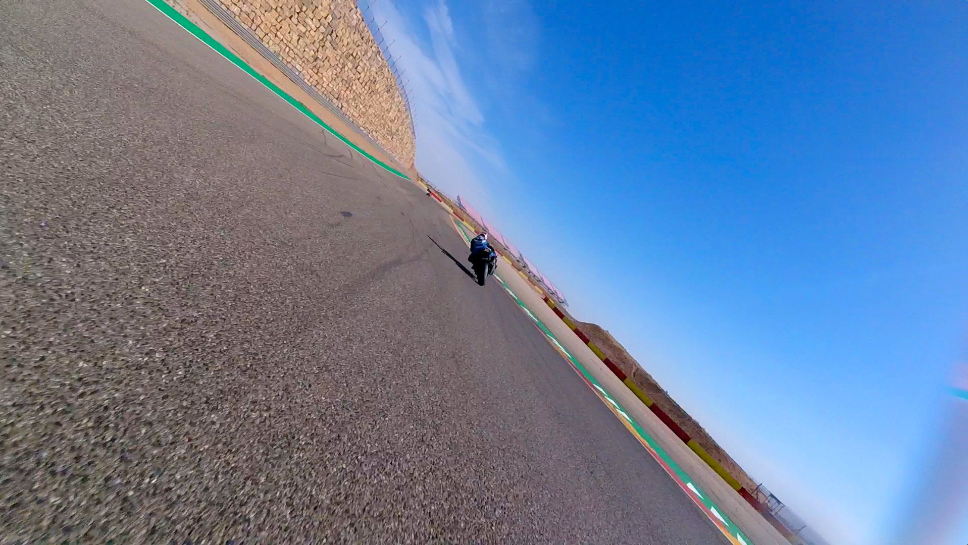 Tilted view of a person on a gravel road near a racetrack under a blue sky
