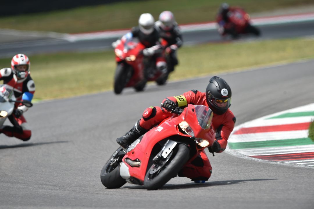 Motorcycle racers lean into a turn on a racetrack, with a red rider in the foreground.