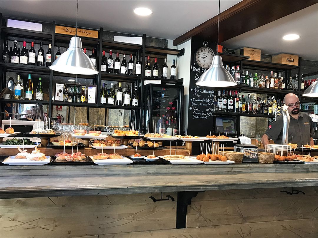 Bar with wine bottles, hanging lights, and a buffet counter with dishes and drinks