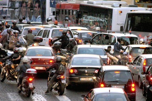 Heavy traffic jam with cars, motorcycles, and buses crowded on a wet city street.