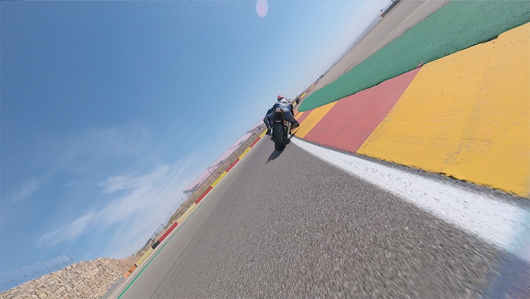 Motorcycle leaning into a turn on a racetrack with red, green, and yellow runoff barriers