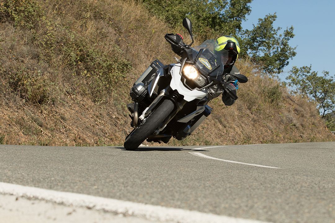 Motorcyclist leaning into a curve on a winding road, wearing a black and neon helmet.