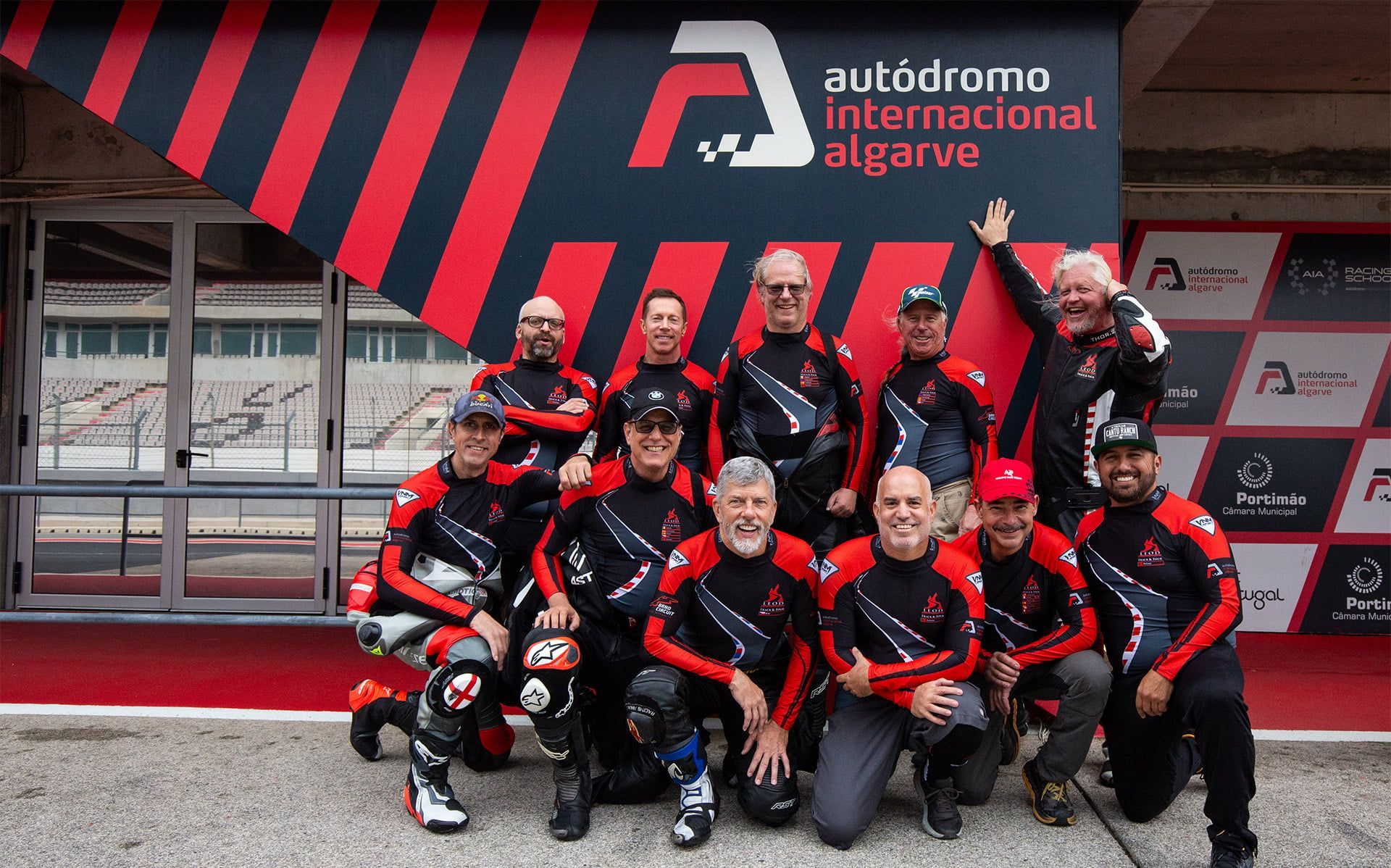 Racing team in red-and-black suits posing outside Autódromo Internacional do Algarve garage