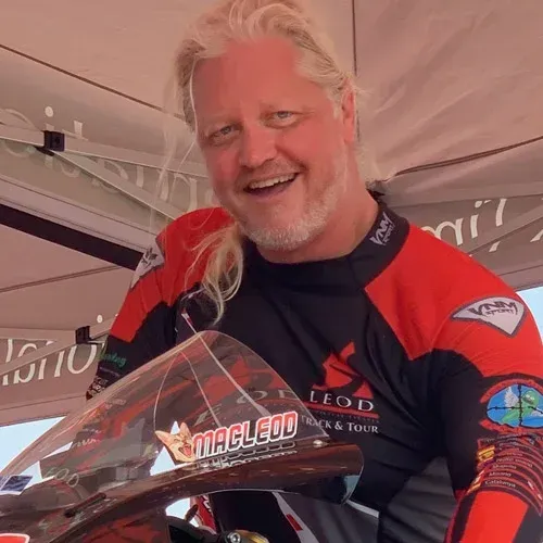 Smiling man in red and black racing jersey holding a clear trophy under a tent