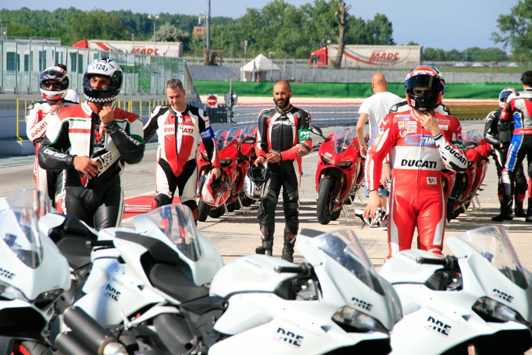 Motorcycle riders in red and black gear standing beside white sport bikes on a racetrack