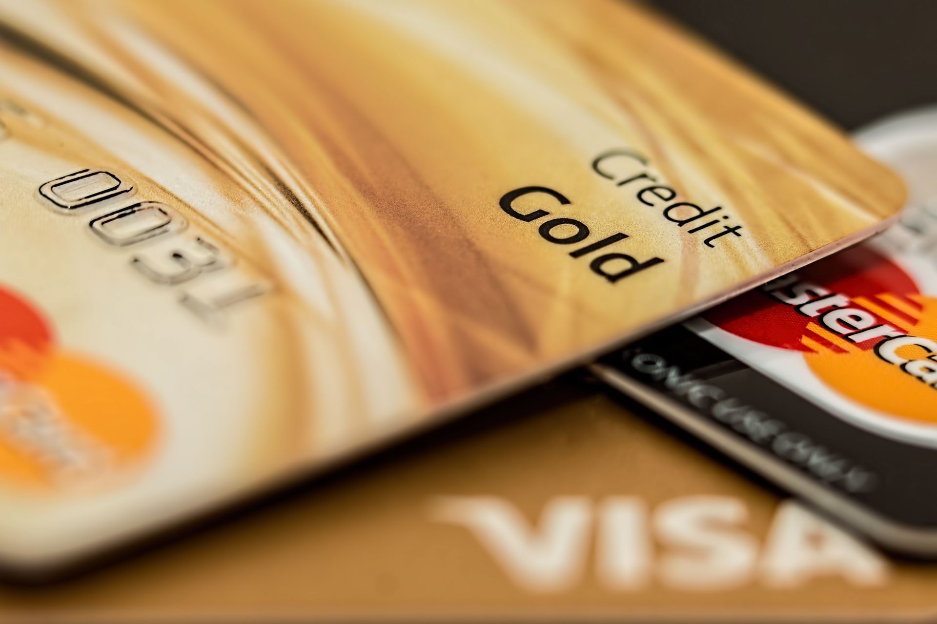 Close-up of a gold credit card and a Visa card overlapping on a warm-toned surface