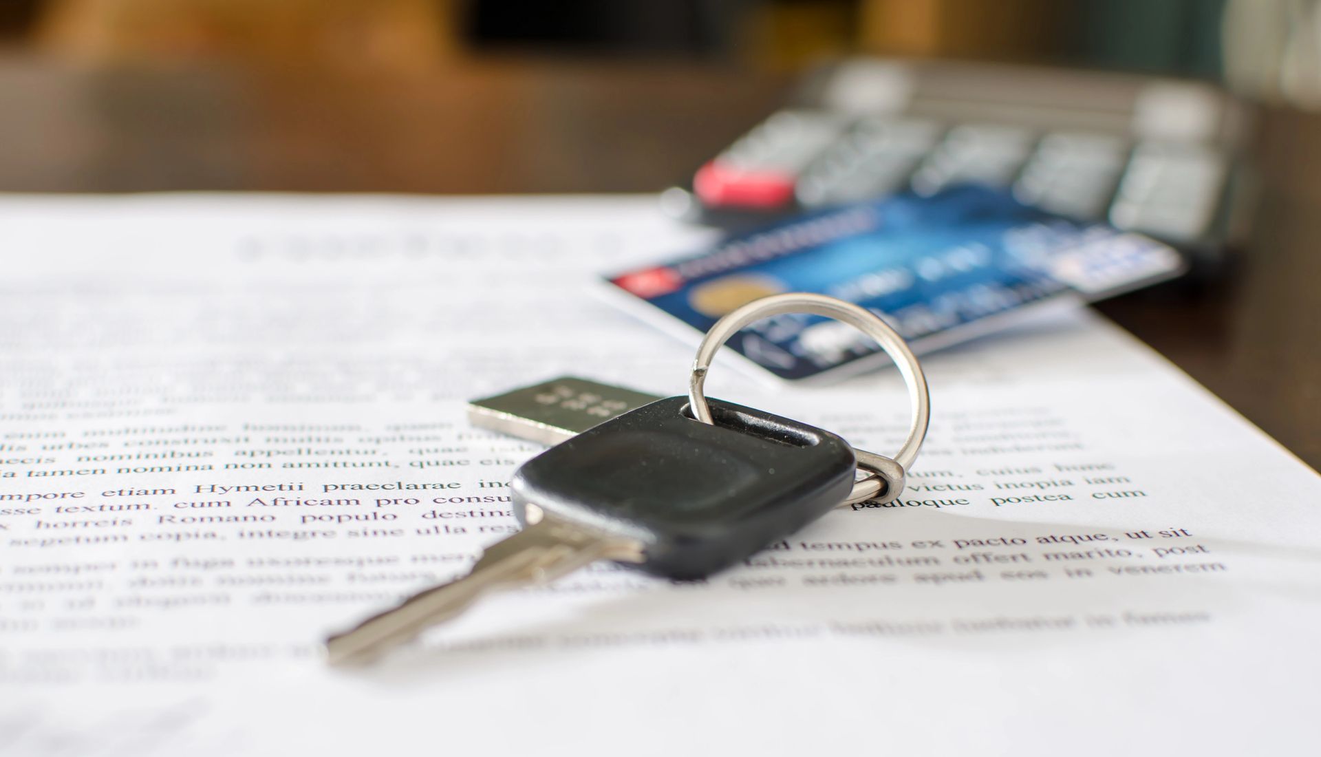 Chiave dell'auto su un documento con carte di credito e una calcolatrice, che suggeriscono i dettagli per l'acquisto dell'auto.