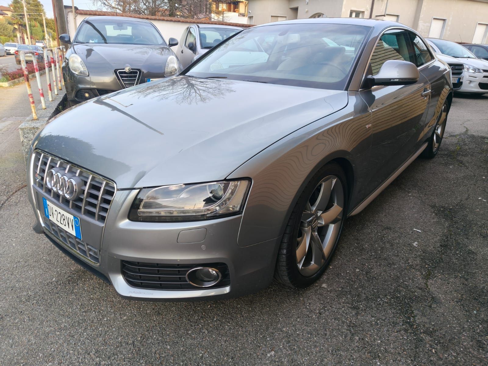 Un'Audi A5 coupé color argento parcheggiata sul marciapiede davanti ad altri veicoli.