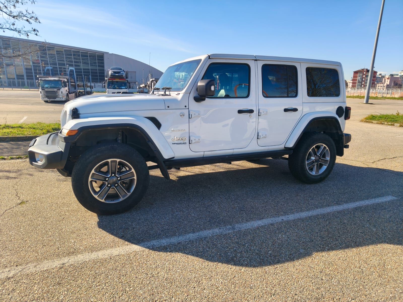 Jeep Wrangler bianca parcheggiata in un piazzale asfaltato in una giornata di sole.